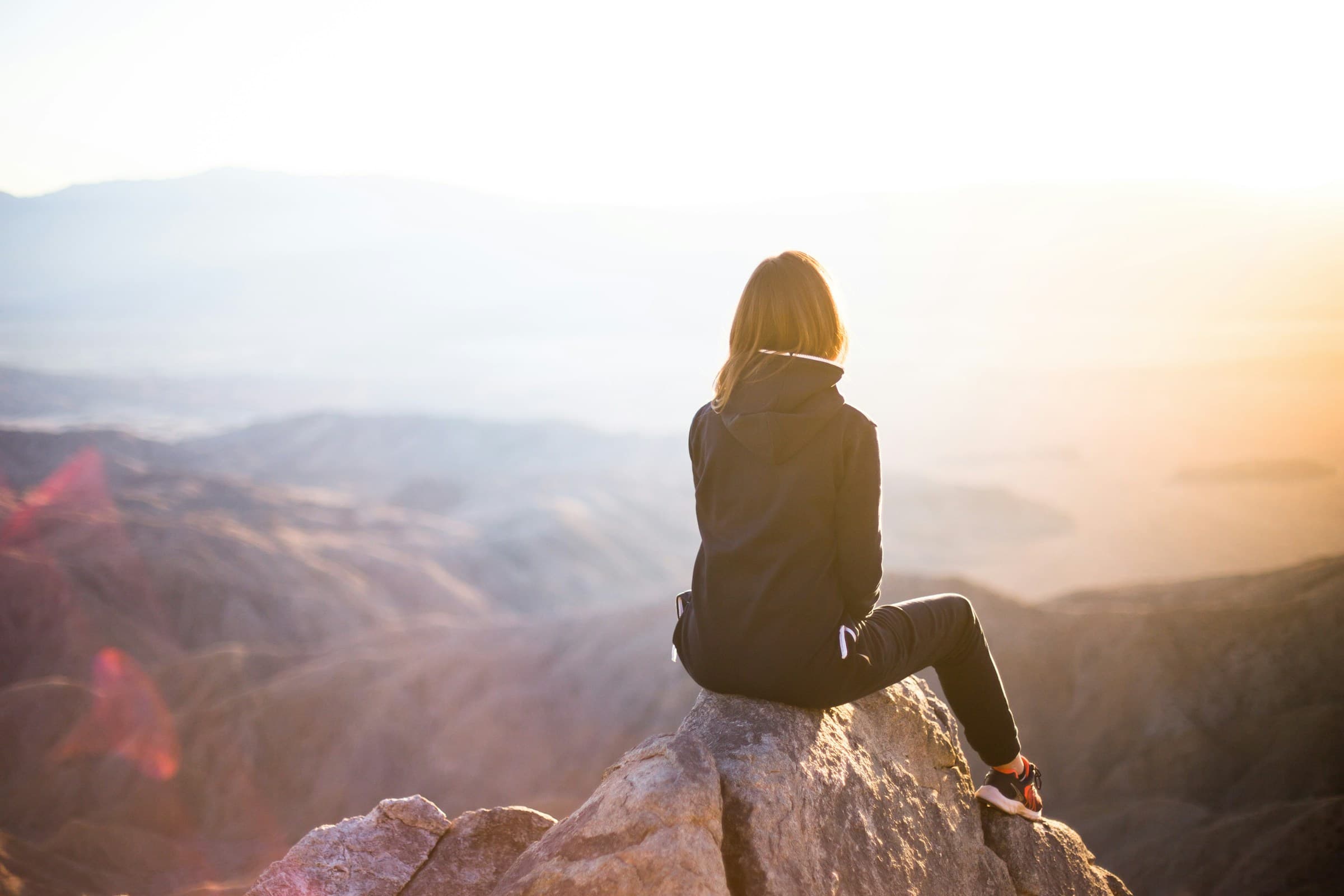 A person sitting on a mountain summit looking over the valley at sunrise